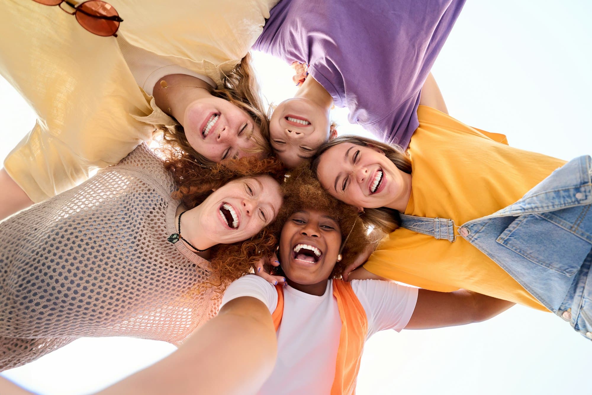 Group of young cheerful multiracial friends looking at camera hugging happy in community.